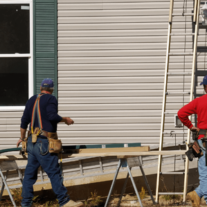 Picture of two siding professionals working on the side of a house with a ladder and tools